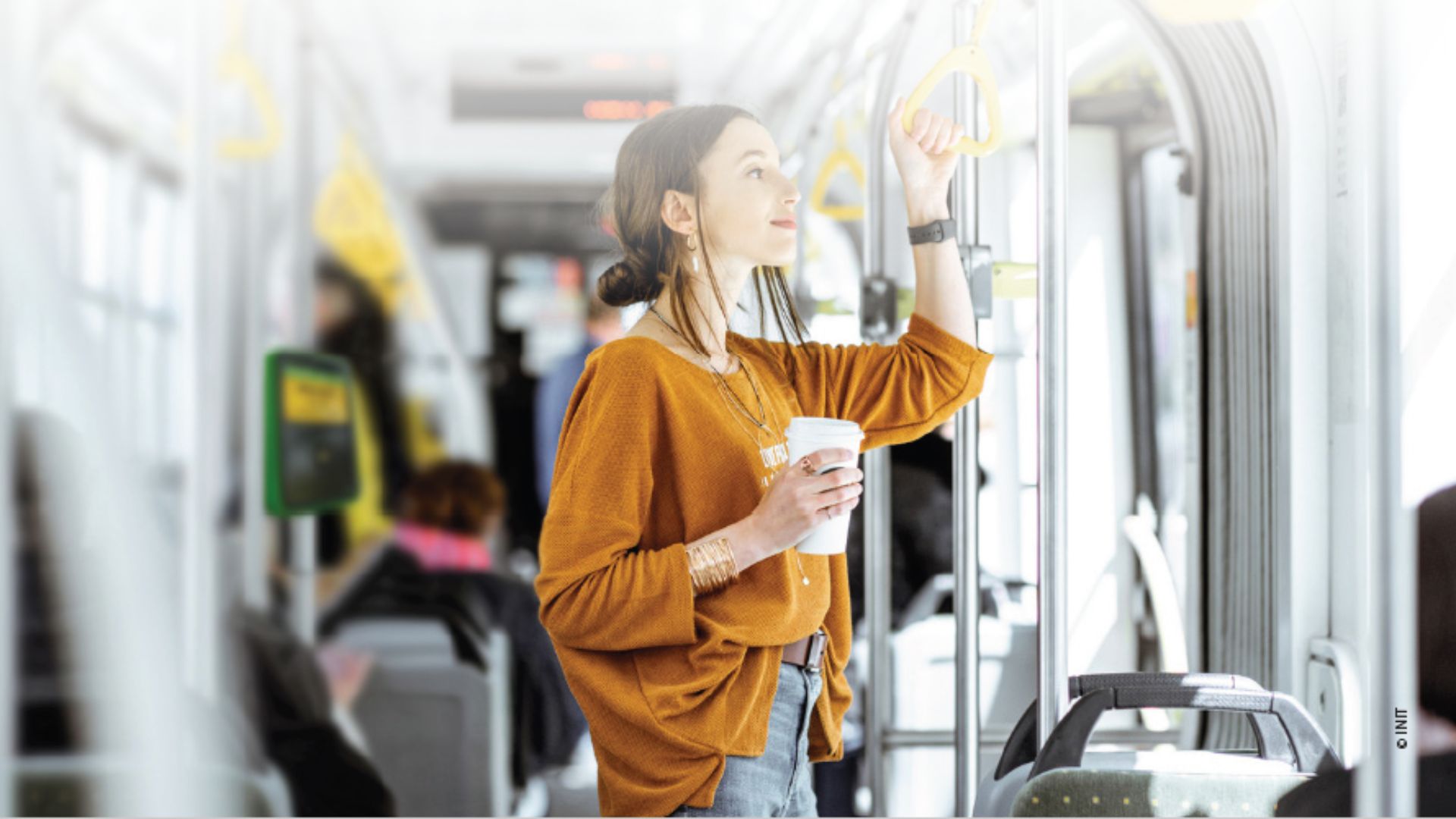 A woman holding a cup of coffee riding a bus.