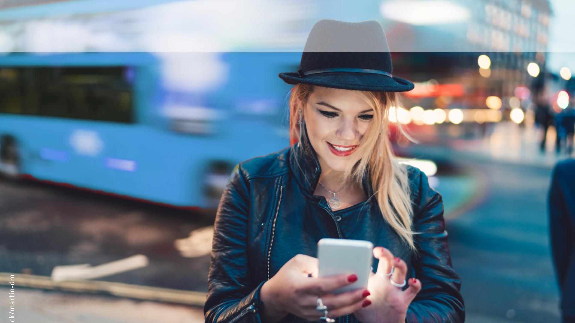 Woman smiling at phone while bus passes in background